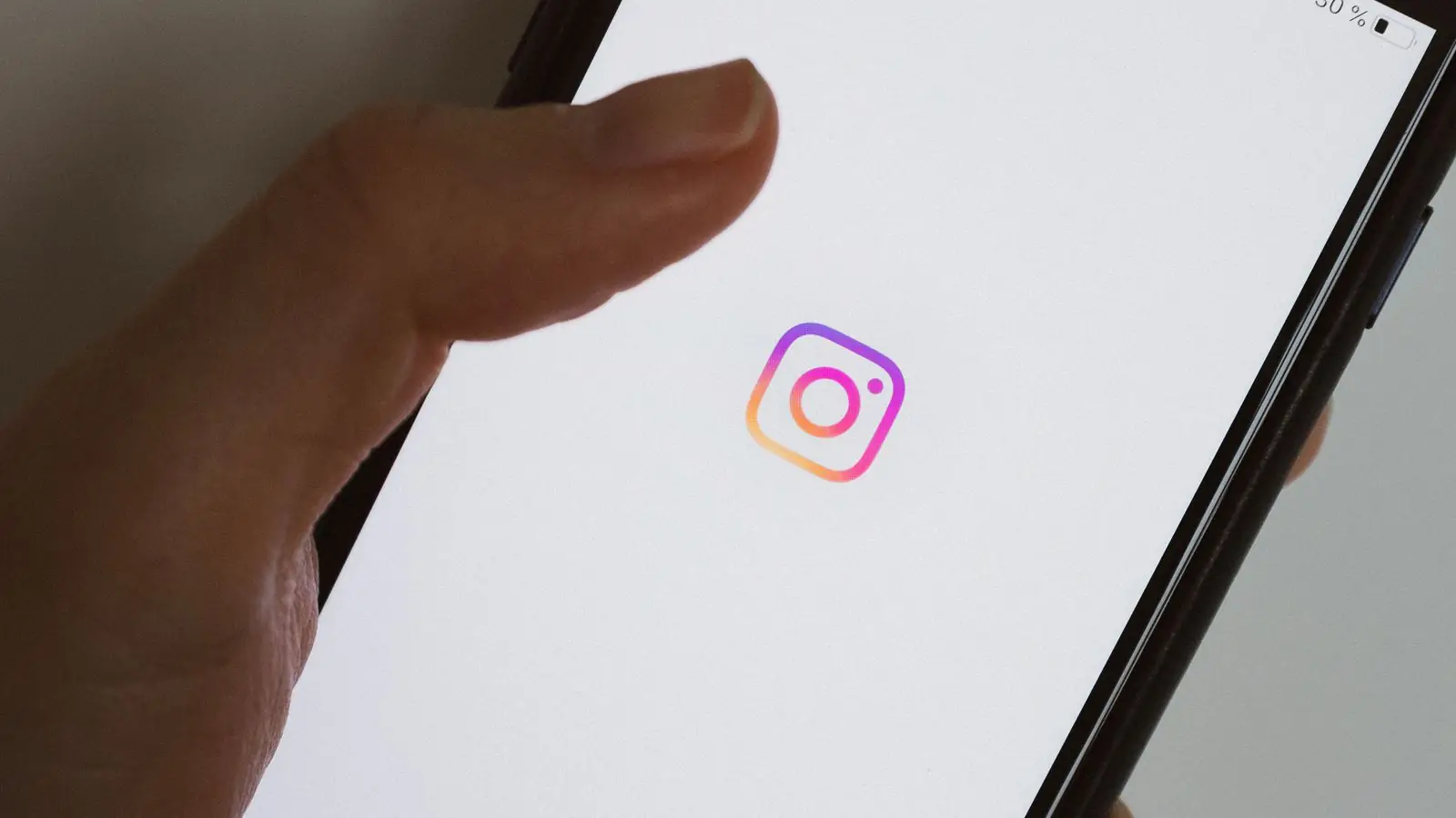 Mână ținând un telefon pe care e deschisă aplicația Instagram
