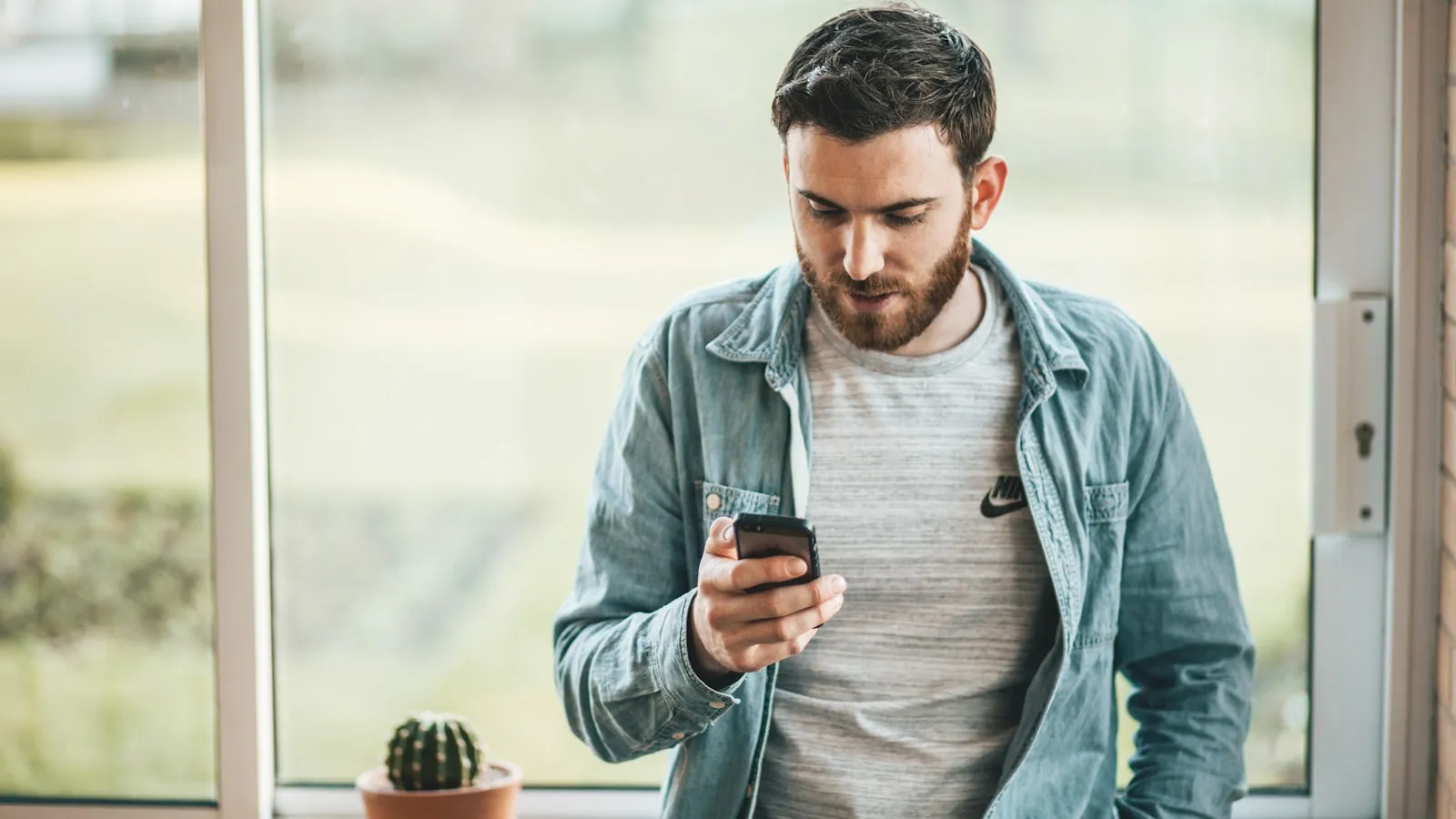 Bărbat lângă fereastră verificând un mesaj pe telefon