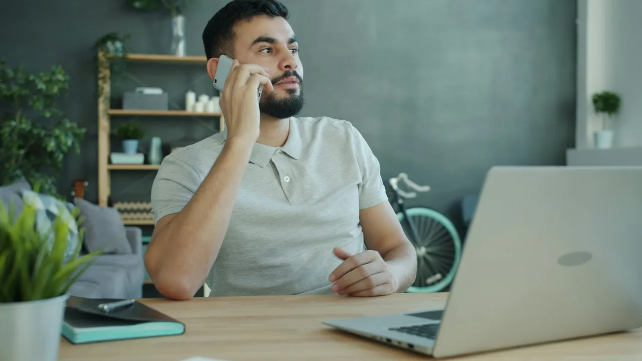 Bărbat la birou vorbind la telefon, cu laptopul deschis în față