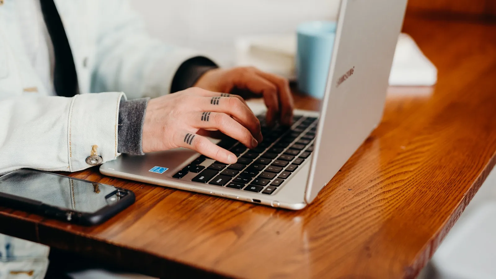Mâini tastând pe un laptop la birou, cu telefonul alături pe masă