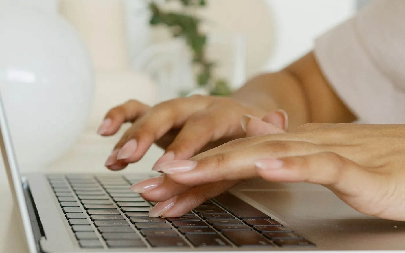 Mâini care tastează pe tastatura unui laptop, într-un birou luminos
